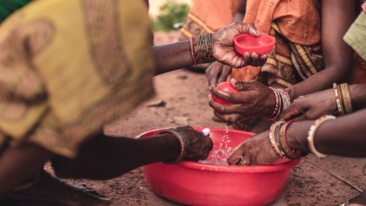 about-01 South Asian women washing hands with bowls, showcasing traditional wear and cultural practices in Odisha, India.